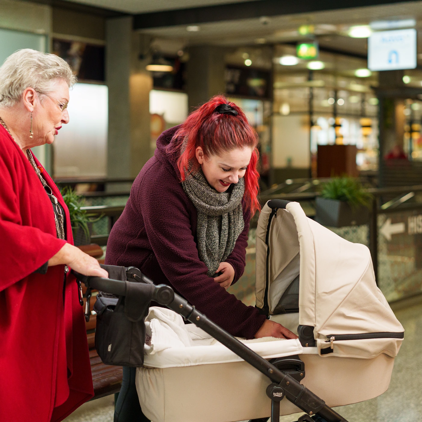 Two visitors with a pram inside Kauppapaikka Tavastila, with a sign pointing to the lifts in the background